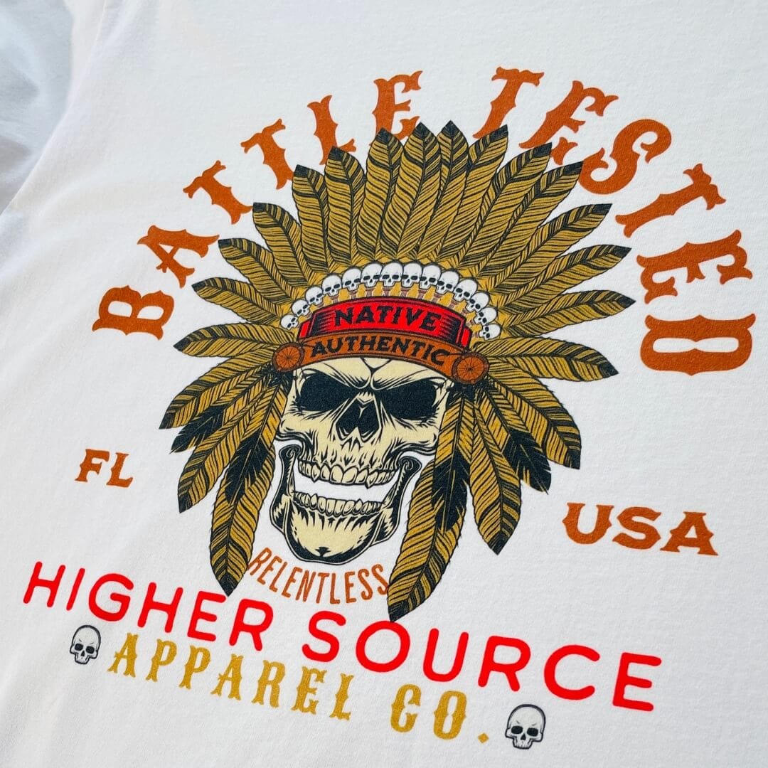 A white higher source apparel t shirt with battle tested in large font surrounding an apache skull with feathers. Higher source apparel co is written below in red font along with FL and USA.