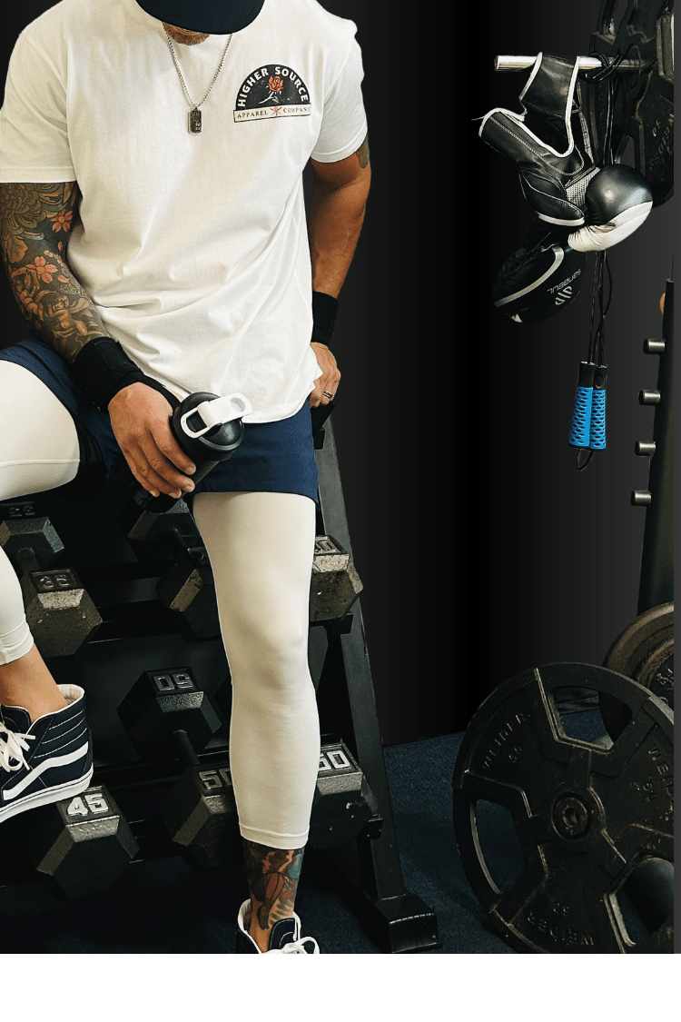 Image of a man leaning on a weight rack with a white higher source apparel t shirt on.  