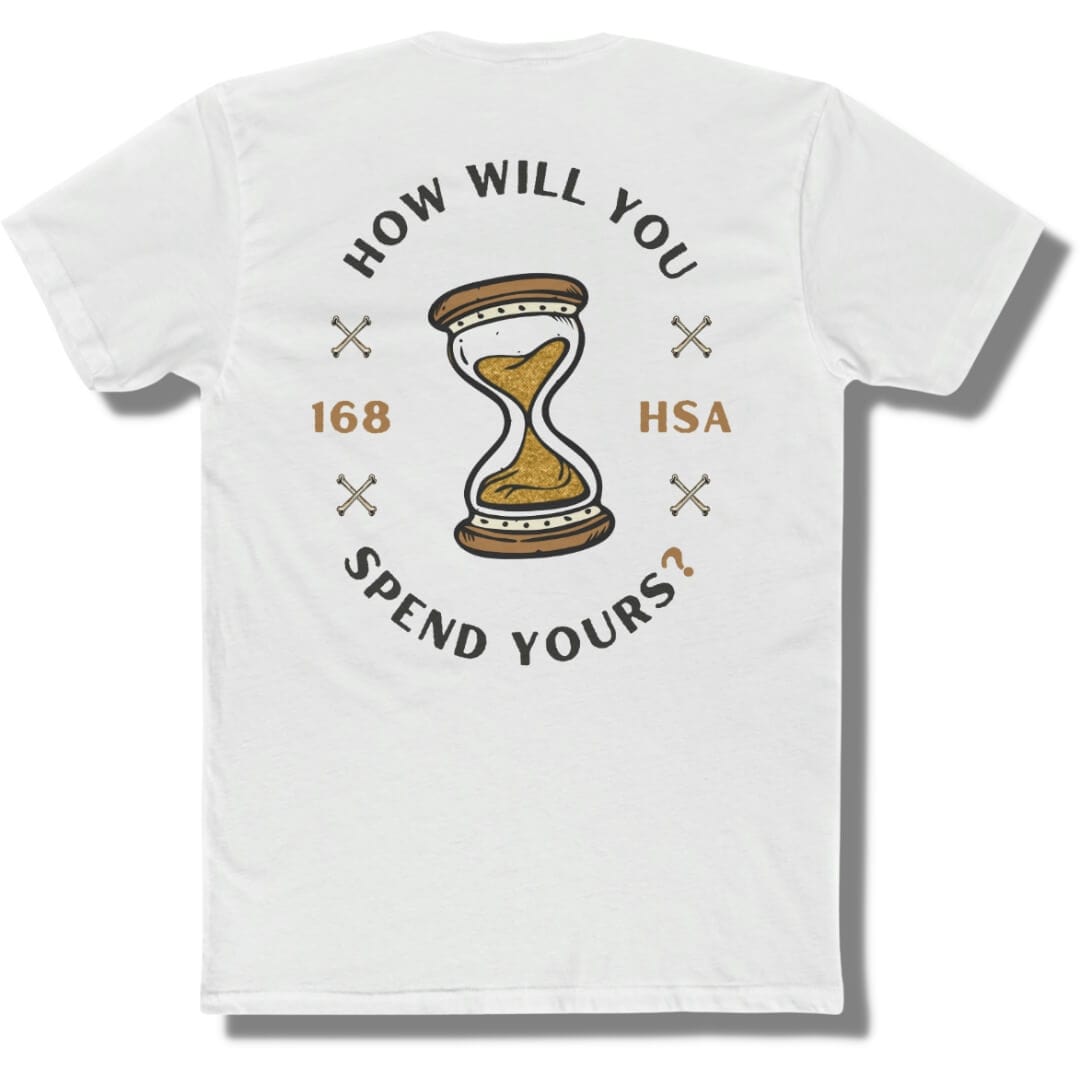 Back side of a white t shirt with "how will you spend yours" in an oval shape. The font is in black and gold with an hour glass in the center.